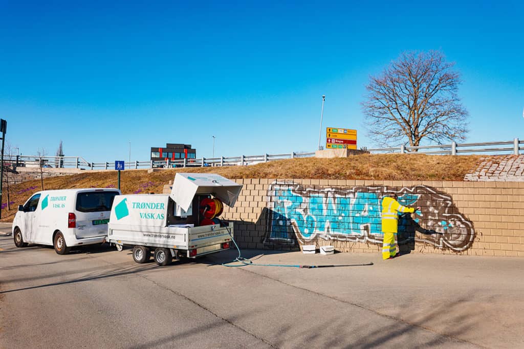 Trøndervask-bil og grafittifjerningsutstyr. Mann fjerner grafitti på mur.
